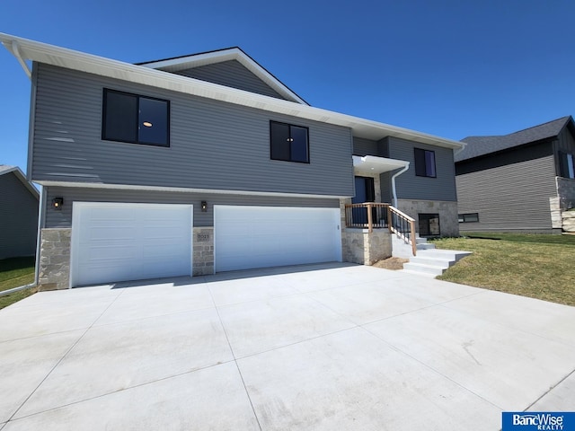 view of front of house featuring a garage, stone siding, driveway, and a front yard