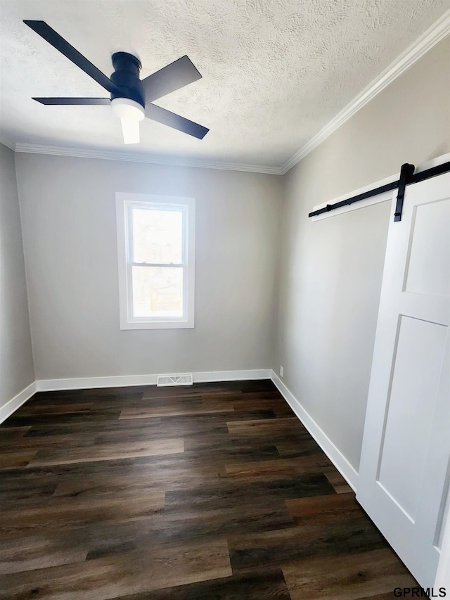 empty room with dark wood-type flooring, ornamental molding, a barn door, and a textured ceiling