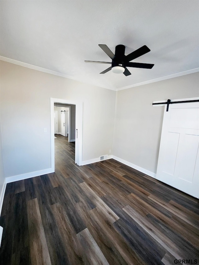 spare room featuring dark wood-type flooring, ornamental molding, and a barn door