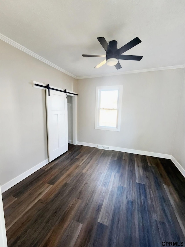 unfurnished bedroom featuring crown molding, dark hardwood / wood-style floors, ceiling fan, and a barn door