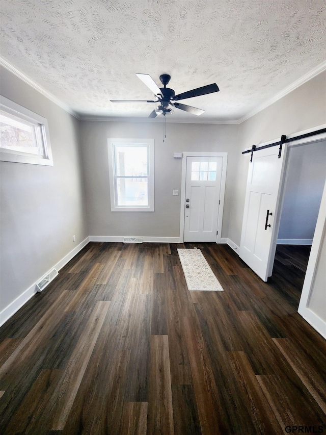 entrance foyer featuring ceiling fan, crown molding, a barn door, dark wood-type flooring, and a textured ceiling