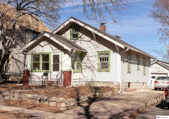 bungalow with an outbuilding, roof with shingles, driveway, and a chimney