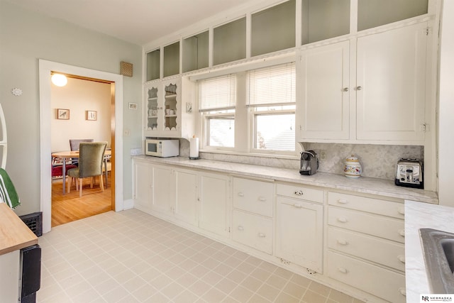 kitchen featuring glass insert cabinets, a sink, decorative backsplash, and white microwave