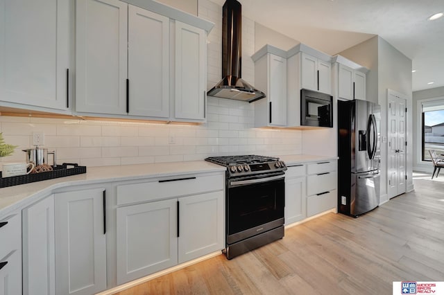 kitchen featuring appliances with stainless steel finishes, white cabinetry, decorative backsplash, wall chimney exhaust hood, and light wood-type flooring