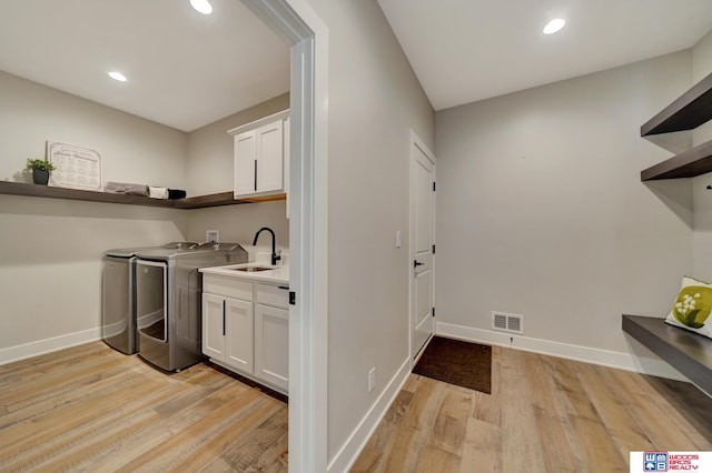 clothes washing area with cabinets, sink, washing machine and clothes dryer, and light hardwood / wood-style flooring