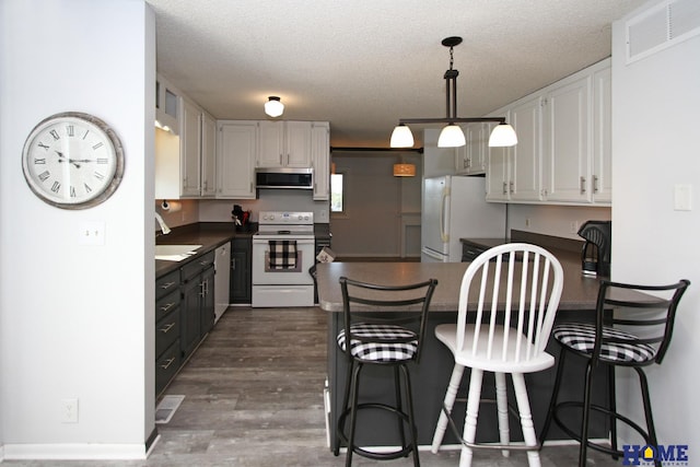 kitchen with white cabinets, white appliances, a textured ceiling, and a kitchen bar