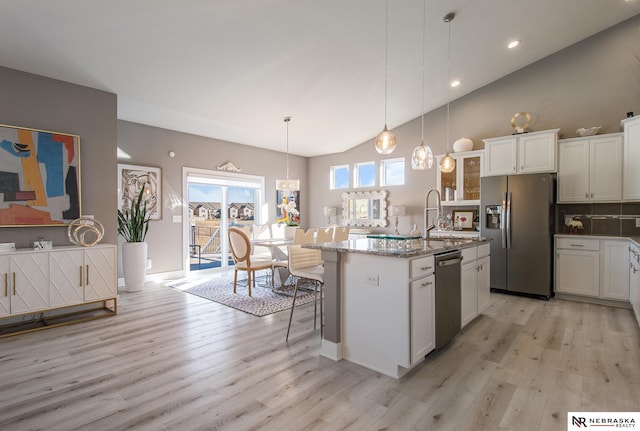 kitchen with pendant lighting, stone counters, white cabinetry, stainless steel appliances, and an island with sink