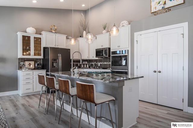 kitchen with white cabinetry, stainless steel appliances, a kitchen breakfast bar, and an island with sink