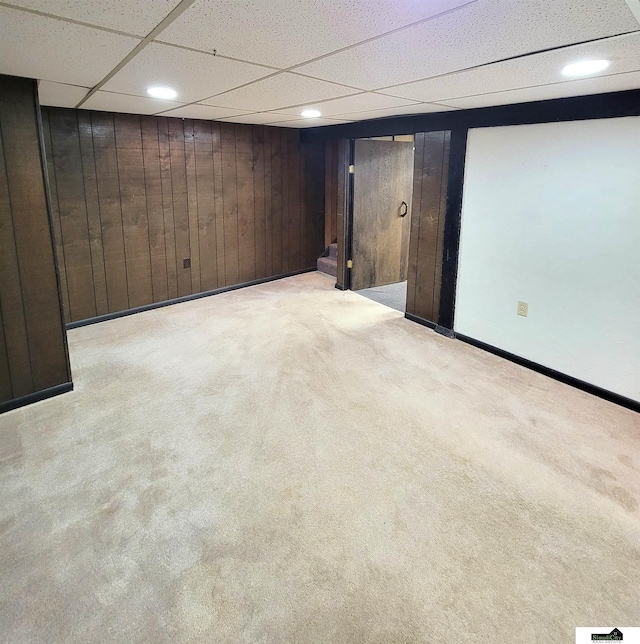 basement with a paneled ceiling, light colored carpet, and wooden walls