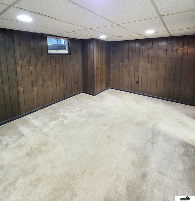 basement featuring light carpet, a paneled ceiling, and wood walls