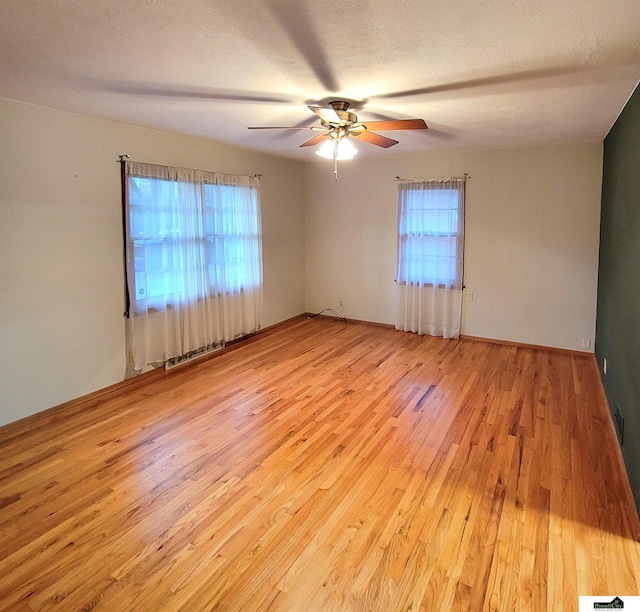 empty room featuring ceiling fan, a wealth of natural light, light hardwood / wood-style floors, and a textured ceiling