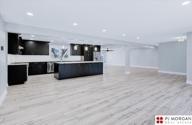 kitchen with hanging light fixtures, appliances with stainless steel finishes, a kitchen island, light hardwood / wood-style floors, and decorative backsplash