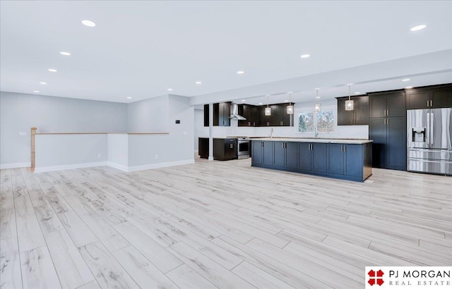 kitchen with wall chimney range hood, appliances with stainless steel finishes, hanging light fixtures, light hardwood / wood-style floors, and a kitchen island