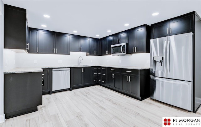 kitchen with stainless steel appliances, light stone countertops, sink, and light hardwood / wood-style flooring