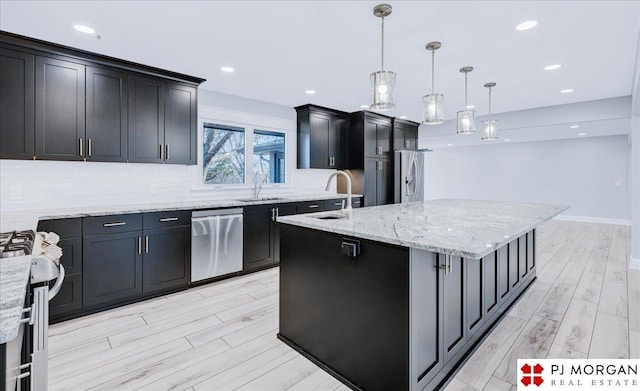 kitchen featuring pendant lighting, sink, appliances with stainless steel finishes, a center island with sink, and light wood-type flooring