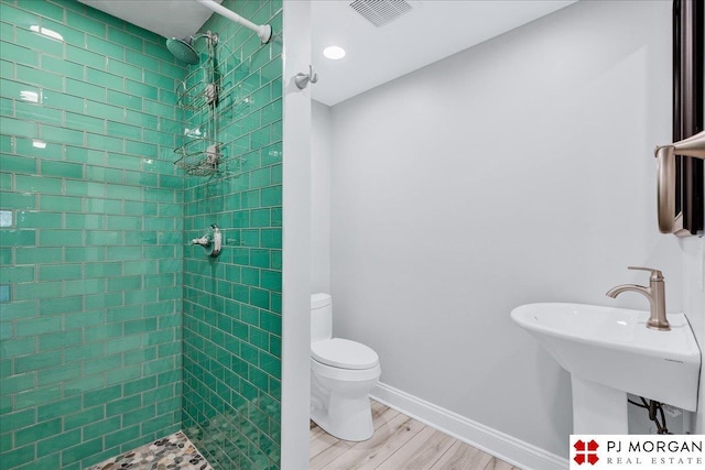 bathroom featuring hardwood / wood-style flooring, toilet, and tiled shower