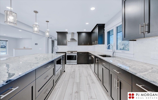 kitchen featuring sink, backsplash, hanging light fixtures, stainless steel appliances, and wall chimney range hood