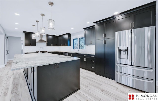 kitchen featuring decorative light fixtures, sink, a kitchen island with sink, stainless steel fridge with ice dispenser, and a barn door