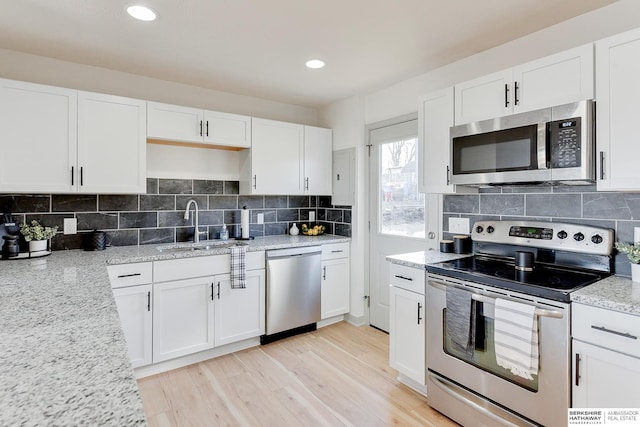 kitchen featuring decorative backsplash, stainless steel appliances, light hardwood / wood-style floors, and white cabinets