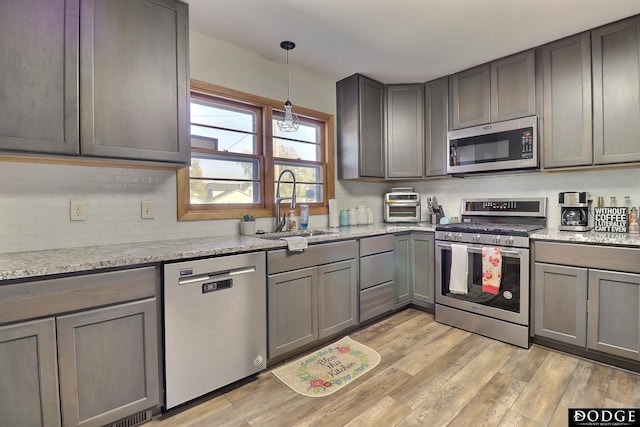 kitchen with decorative light fixtures, sink, light stone counters, stainless steel appliances, and light wood-type flooring