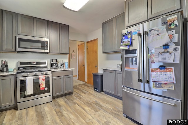 kitchen with light stone counters, gray cabinets, stainless steel appliances, and light wood-type flooring