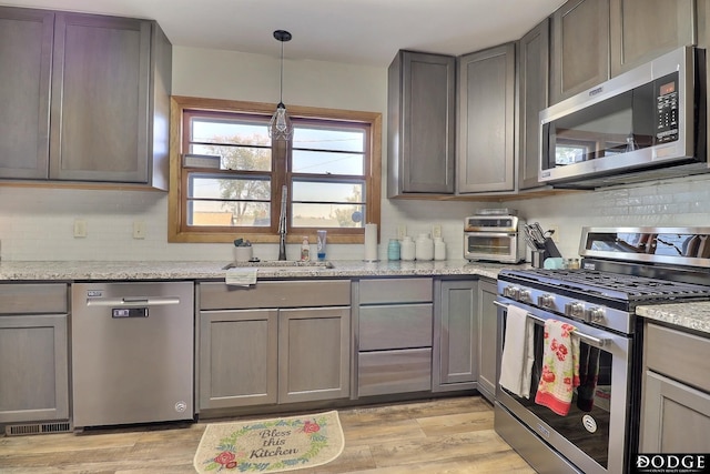 kitchen featuring sink, gray cabinetry, light stone counters, stainless steel appliances, and light wood-type flooring