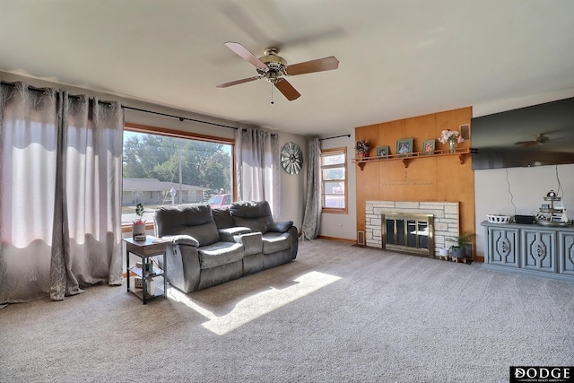 carpeted living room with a stone fireplace and ceiling fan