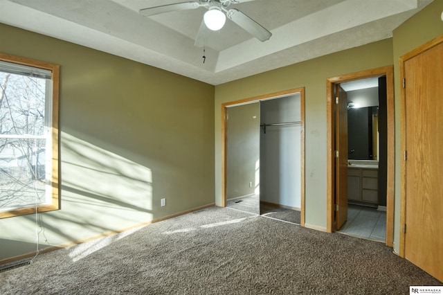 unfurnished bedroom featuring connected bathroom, dark colored carpet, a raised ceiling, a closet, and ceiling fan