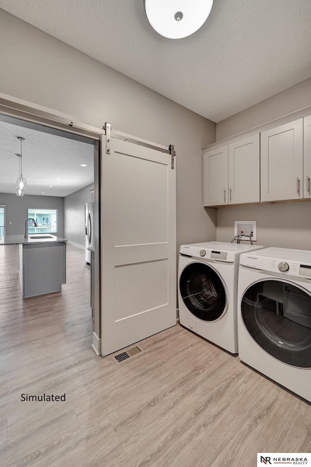 laundry area with washing machine and clothes dryer, cabinets, a textured ceiling, light wood-type flooring, and a barn door