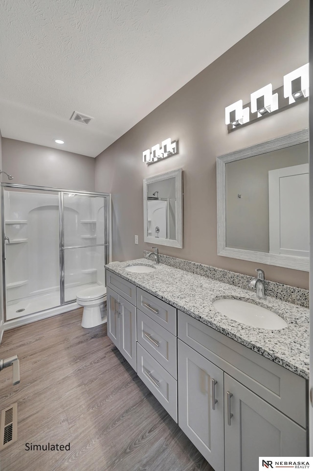 bathroom with hardwood / wood-style flooring, vanity, a textured ceiling, a shower with shower door, and toilet