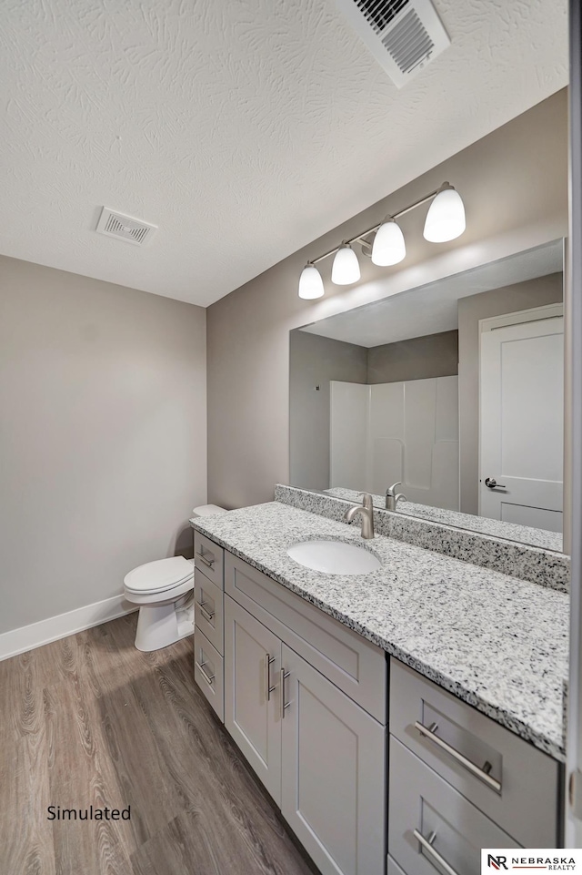 bathroom with wood-type flooring, vanity, walk in shower, toilet, and a textured ceiling