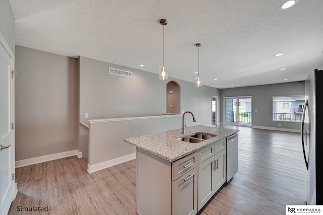 kitchen with pendant lighting, sink, stainless steel appliances, light stone countertops, and a center island with sink