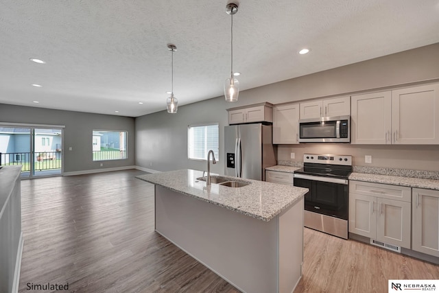 kitchen featuring plenty of natural light, decorative light fixtures, sink, stainless steel appliances, and light stone countertops