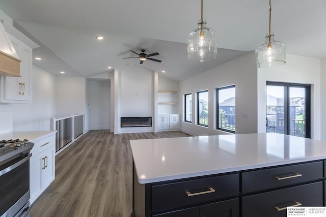 kitchen with a kitchen island, lofted ceiling, white cabinets, hanging light fixtures, and stainless steel range oven