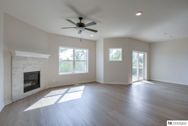 unfurnished living room featuring ceiling fan, a stone fireplace, a wealth of natural light, and light hardwood / wood-style floors