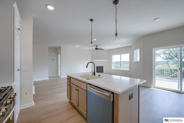 kitchen with appliances with stainless steel finishes, a fireplace, sink, light hardwood / wood-style floors, and a center island with sink