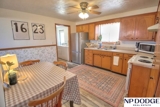 kitchen with washer / dryer, sink, ceiling fan, stainless steel appliances, and light hardwood / wood-style flooring