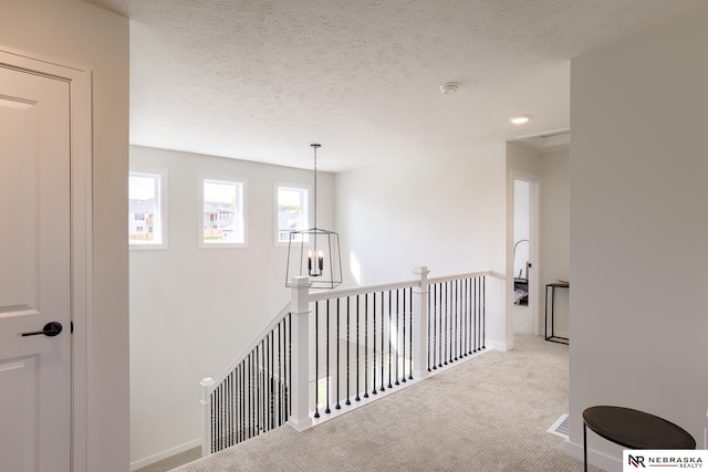 corridor with light colored carpet, a notable chandelier, and a textured ceiling