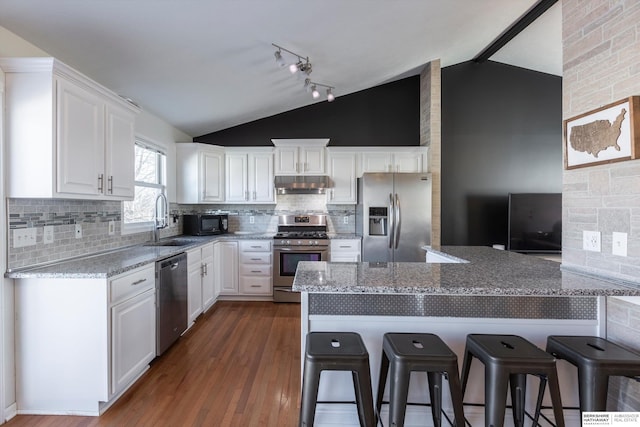 kitchen with a breakfast bar, white cabinetry, light stone counters, lofted ceiling with beams, and appliances with stainless steel finishes