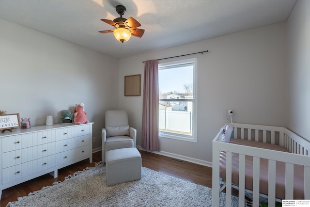 bedroom featuring ceiling fan, a nursery area, and dark hardwood / wood-style flooring