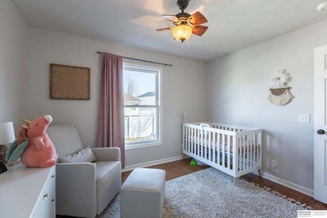 bedroom featuring dark wood-type flooring, ceiling fan, and a nursery area