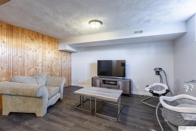 living room with dark wood-type flooring, wooden walls, and a textured ceiling