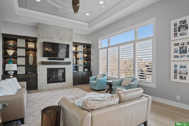 living room with a tray ceiling, a stone fireplace, and light hardwood / wood-style floors