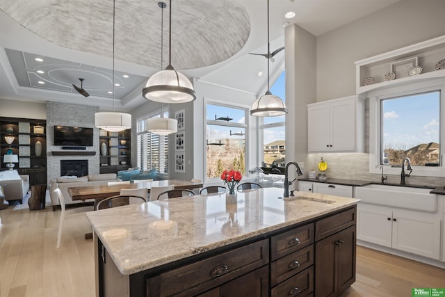 kitchen featuring hanging light fixtures, a fireplace, white cabinets, and a center island with sink