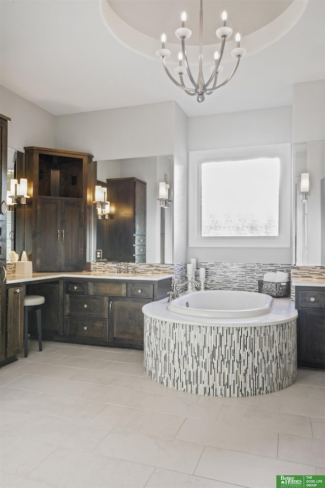 bathroom with vanity, tiled tub, a tray ceiling, and a chandelier