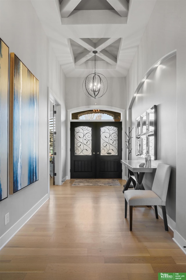 foyer entrance featuring coffered ceiling, light wood-type flooring, a notable chandelier, beam ceiling, and a high ceiling