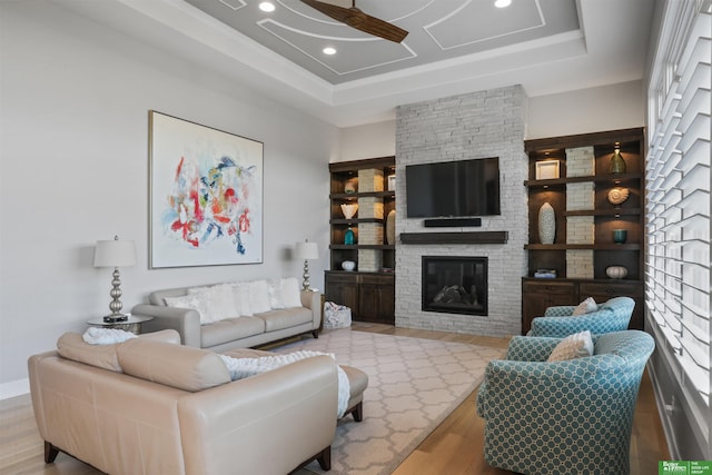 living room with ceiling fan, a fireplace, a raised ceiling, and light hardwood / wood-style floors