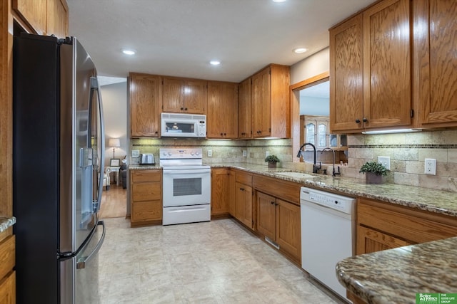 kitchen with light stone counters, white appliances, sink, and backsplash