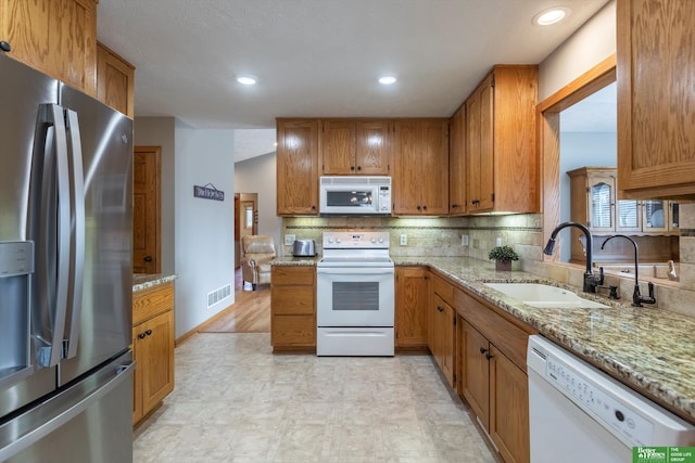 kitchen featuring tasteful backsplash, sink, light stone counters, and white appliances