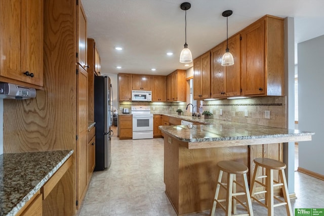 kitchen with a breakfast bar, sink, decorative backsplash, kitchen peninsula, and white appliances